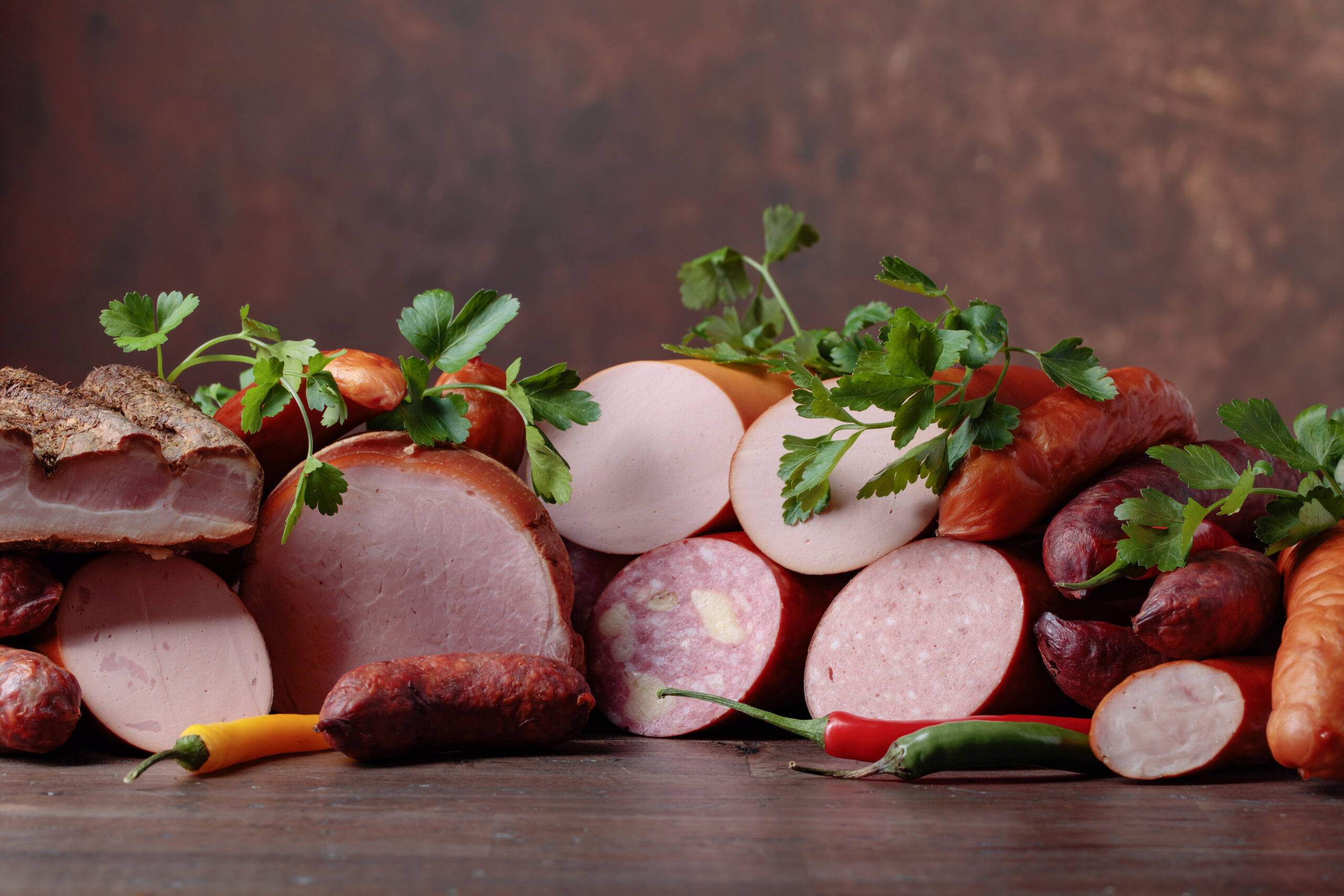 A professional display of various processed meats, including cured salami, hams, and sausages, colored with BioconColors high-stability natural colorants for meat.